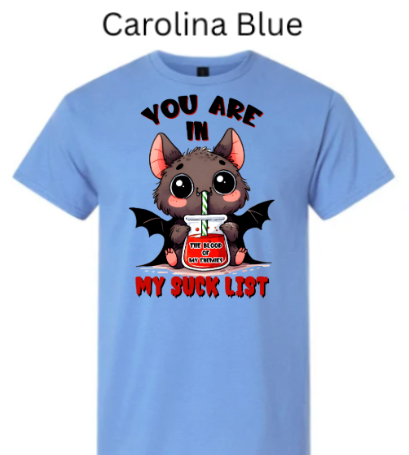 "Light carolina blue t-shirt featuring kawaii vampire bat sipping red drink through straw, jar reads 'The Blood of My Enemies,' 'You Are In My Suck List' text, cute spooky Halloween"