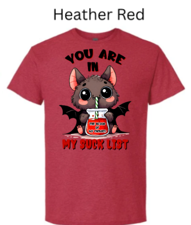 "Red heather t-shirt displaying kawaii vampire bat design, drinking from glass jar marked 'The Blood of My Enemies,' black text 'You Are In My Suck List,' pink ears and rosy cheeks"