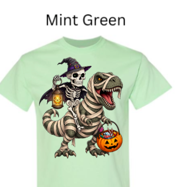 "Mint green t-shirt featuring skeleton witch perched on mummy dinosaur, T-Rex with big green eyes, pumpkin lanterns and treat basket, whimsical Halloween graphic"